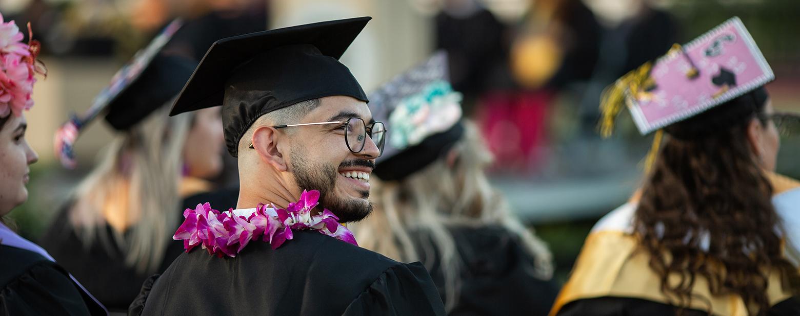 照片中，一名太阳城娱乐的毕业生戴着学士帽，穿着学士服，望着乌鸦. 